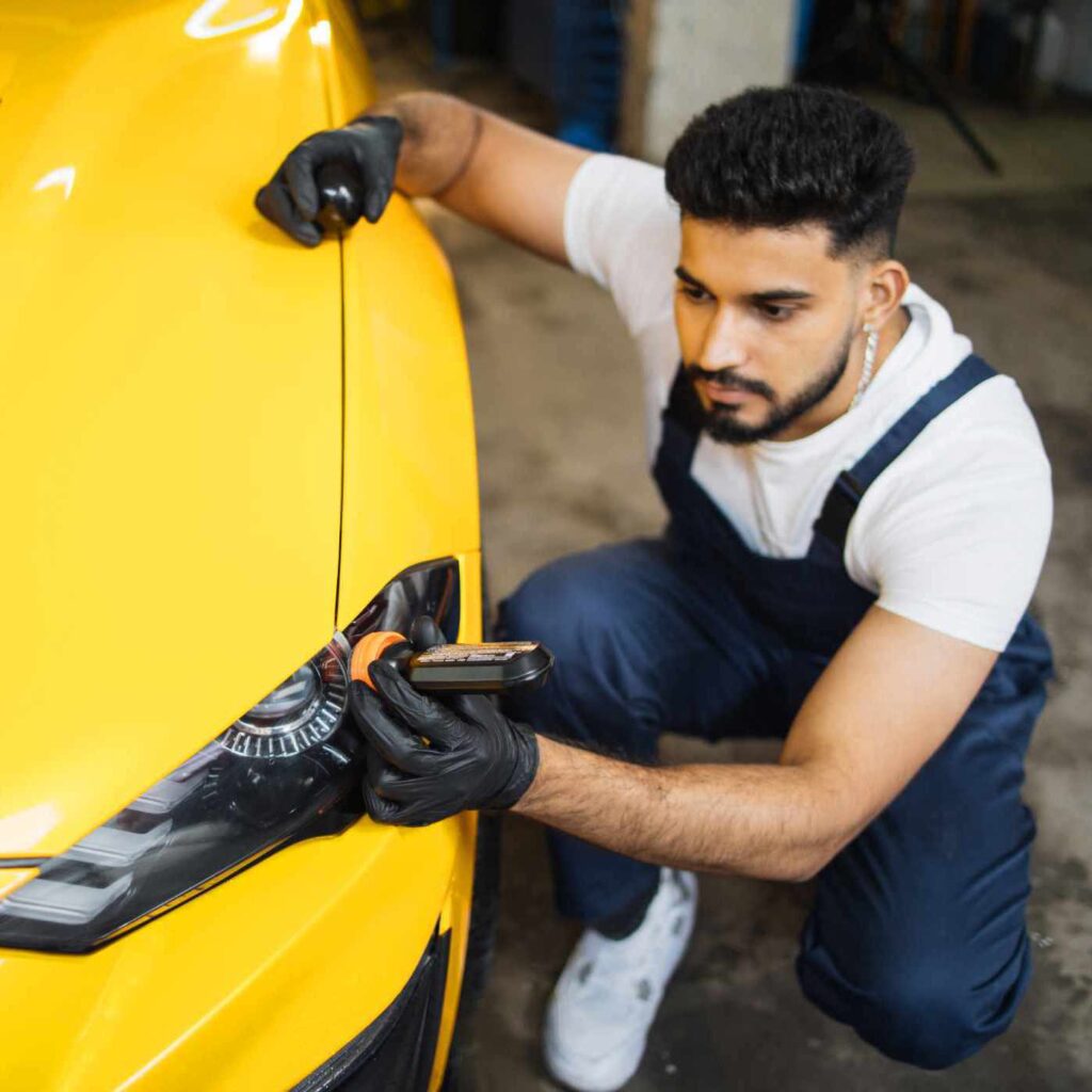 Anti rain coating at auto service. Male worker in blue overalls white t-shirt and protective gloves, on a professional car wash service, applying anti rain coating on a headlight of luxury yellow car.