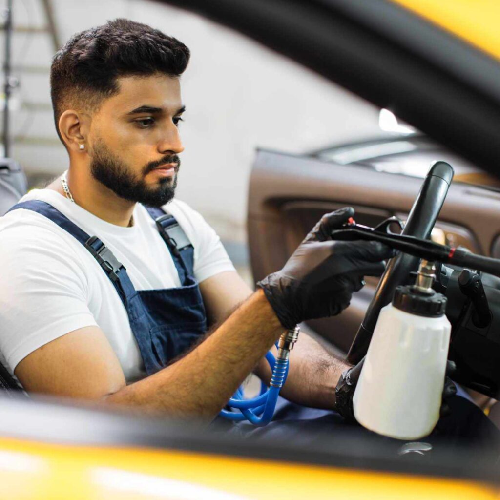 Professional chemical cleaning of interior of yellow luxury cabriolet car by air gun. Male bearded worker of auto service station, cleaning modern vehicle interior with tornado air gun.