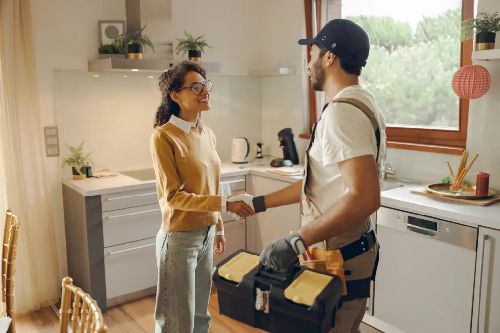 woman-welcoming-repairman-into-kitchen-smiling-h-PR99XTQ